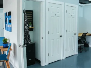 Open micro-office suite number 1 at MicroOffice Solutions Casper Wyoming showing lockable door, filing cabinet, coat hooks, shelving, with community workspace desk and chair visible