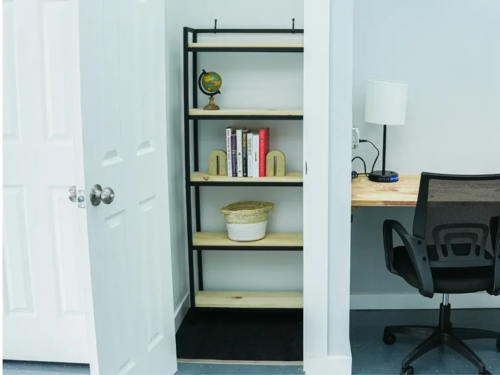MicroOffice Solutions customize suit 3 and workspace Customized micro-office suite at MicroOffice Solutions Casper Wyoming with open lockable door, shelving unit with globe and books, desk lamp. A community workspace with chair is right beside the mincro office suite