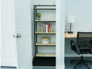 Customized micro-office suite at MicroOffice Solutions Casper Wyoming with open lockable door, shelving unit with globe and books, desk lamp. A community workspace with chair is right beside the mincro office suite