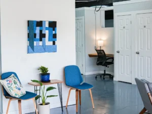 MicroOffice Solutions Casper Wyoming front lobby with blue chairs, plants, abstract wall art and numbered private micro-office suite doors 30, 31 and 32 visible beside a community workspace desk