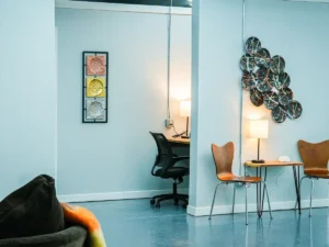 MicroOffice Solutions Casper Wyoming community workspace desk with lamp next to casual client sitting area with wooden chairs and decorative wall art